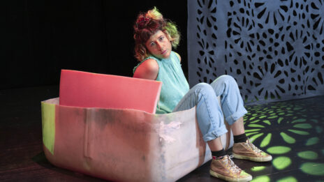 Portrait de Pamina de Coulon qui regarde la caméra. Elle est assise sur un genre de pouf, enfoncée dedans, on ne voit pas tout son corps.