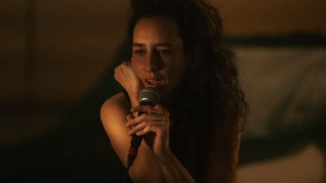 Photo de Racha Baroud. Portrait à partir de la taille, elle a une main contre la joue et tient un micro de l'autre main.