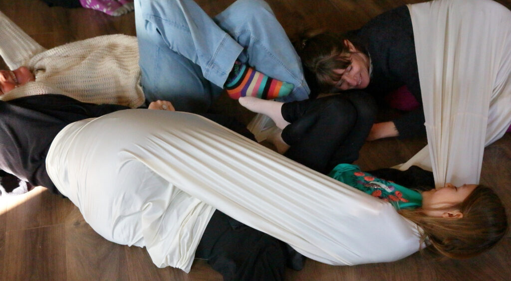 des personnes allongées qui dansent avec un tissu. 